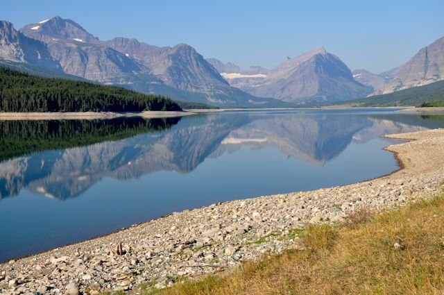 Mountains reflected in reservoir along Many Glacier Road